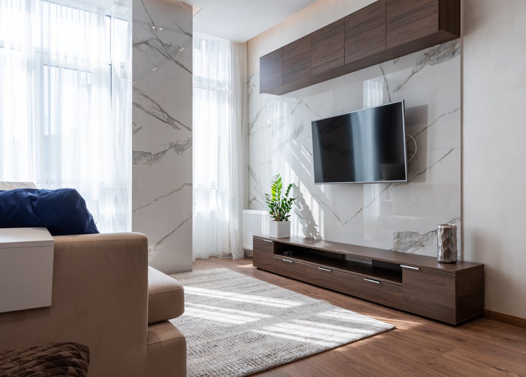 Modern TV set hanging on wall between wooden cabinets in front of comfortable sofa in light living room