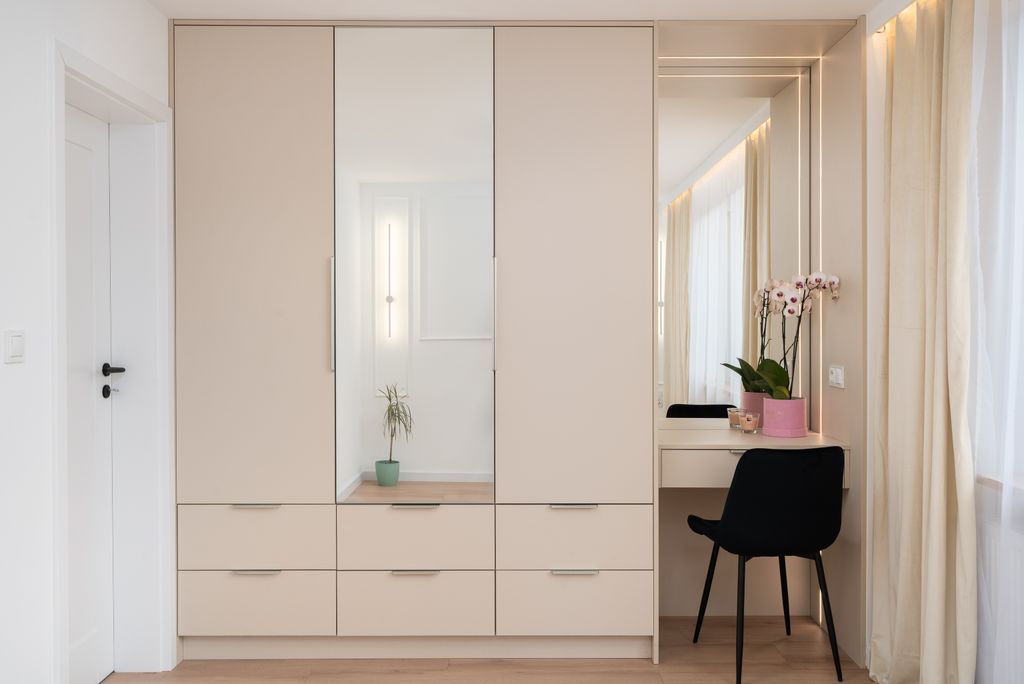 Minimalist bedroom with beige wardrobe and vanity in a bright, elegant setting.